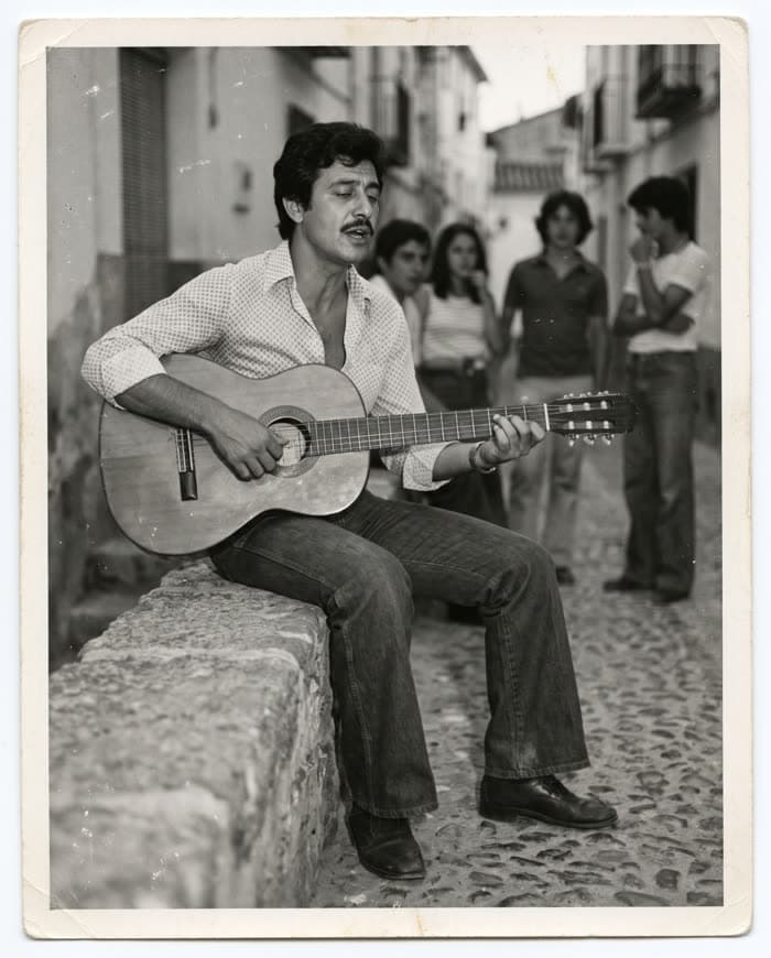 Osvaldo de joven tocando la guitarra en una calle del pueblo, en blanco y negro